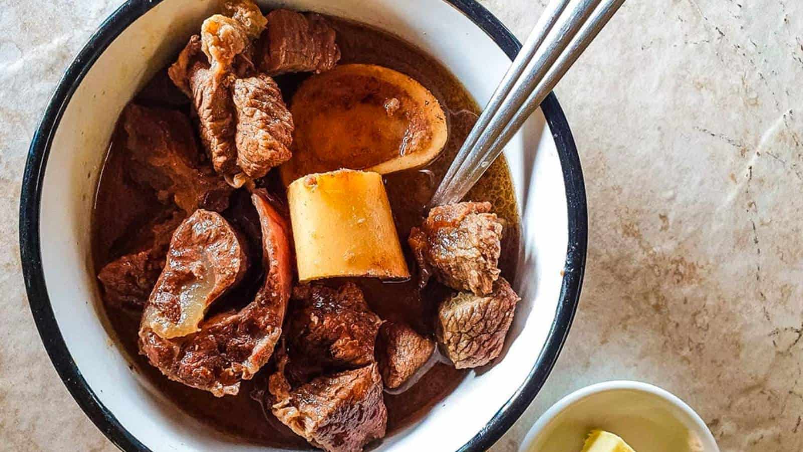 A bowl of beef stew with a spoon and lemon.