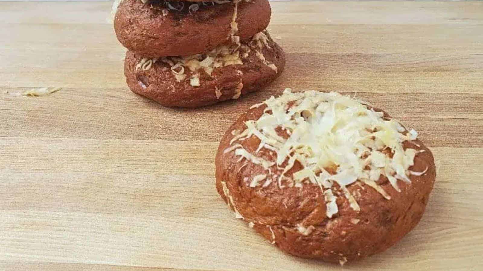Image shows a closeup of Asiago Bagels with one near the front and two stacked behind it.