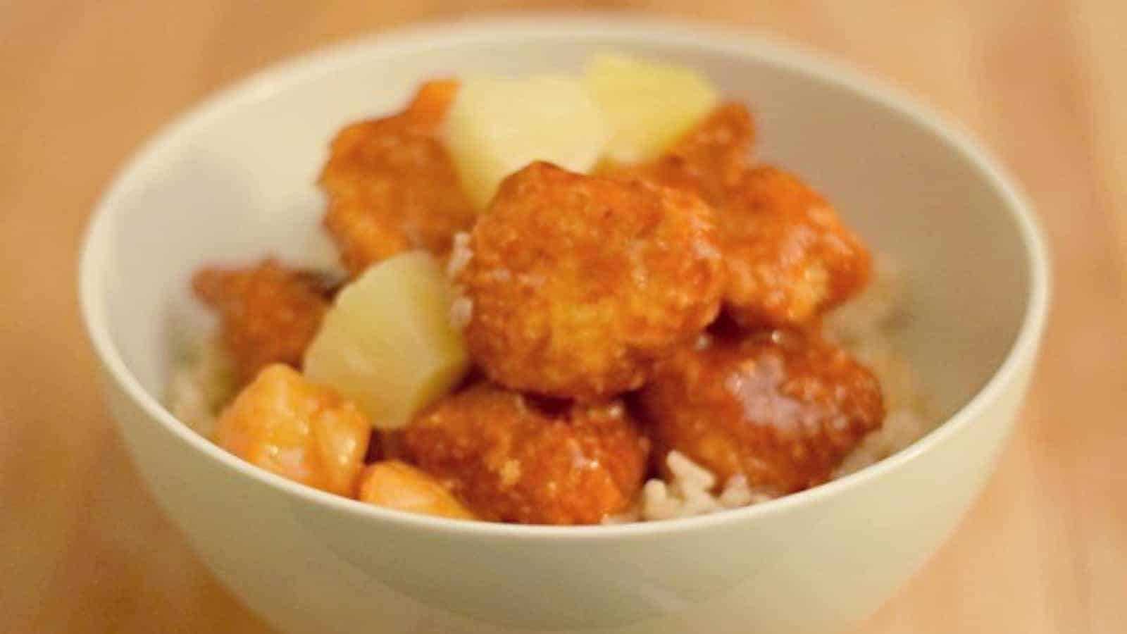 Image shows a Bowl of baked sweet and sour chicken with pineapple.