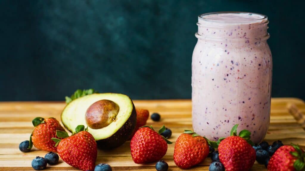 A smoothie with berries and avocado on a wooden cutting board.