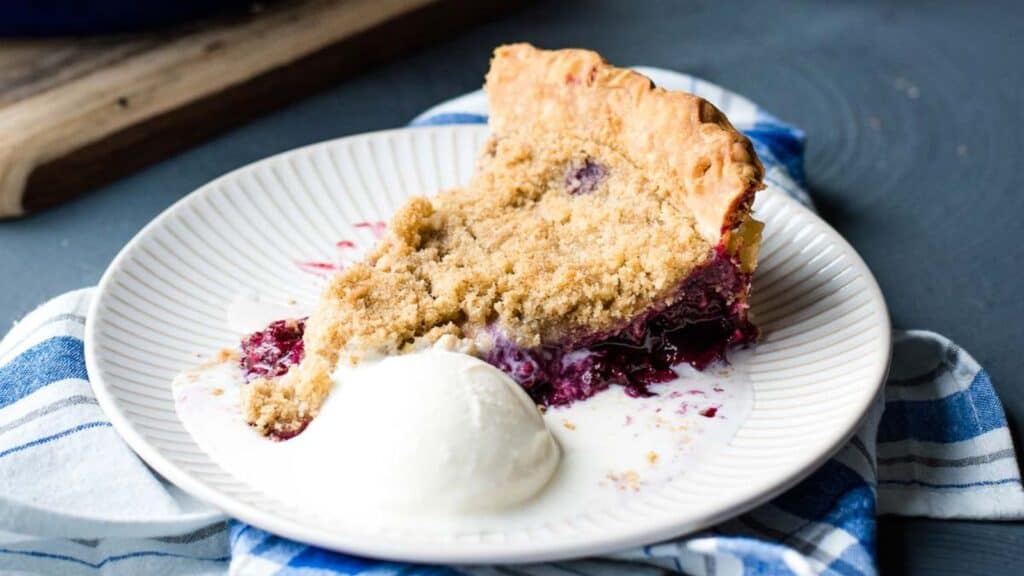 A slice of blackberry crumble pie on a plate with ice cream.