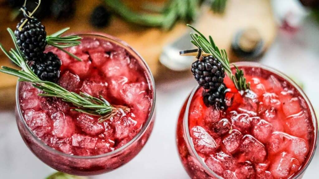 Two glasses with blackberries and rosemary sprigs.