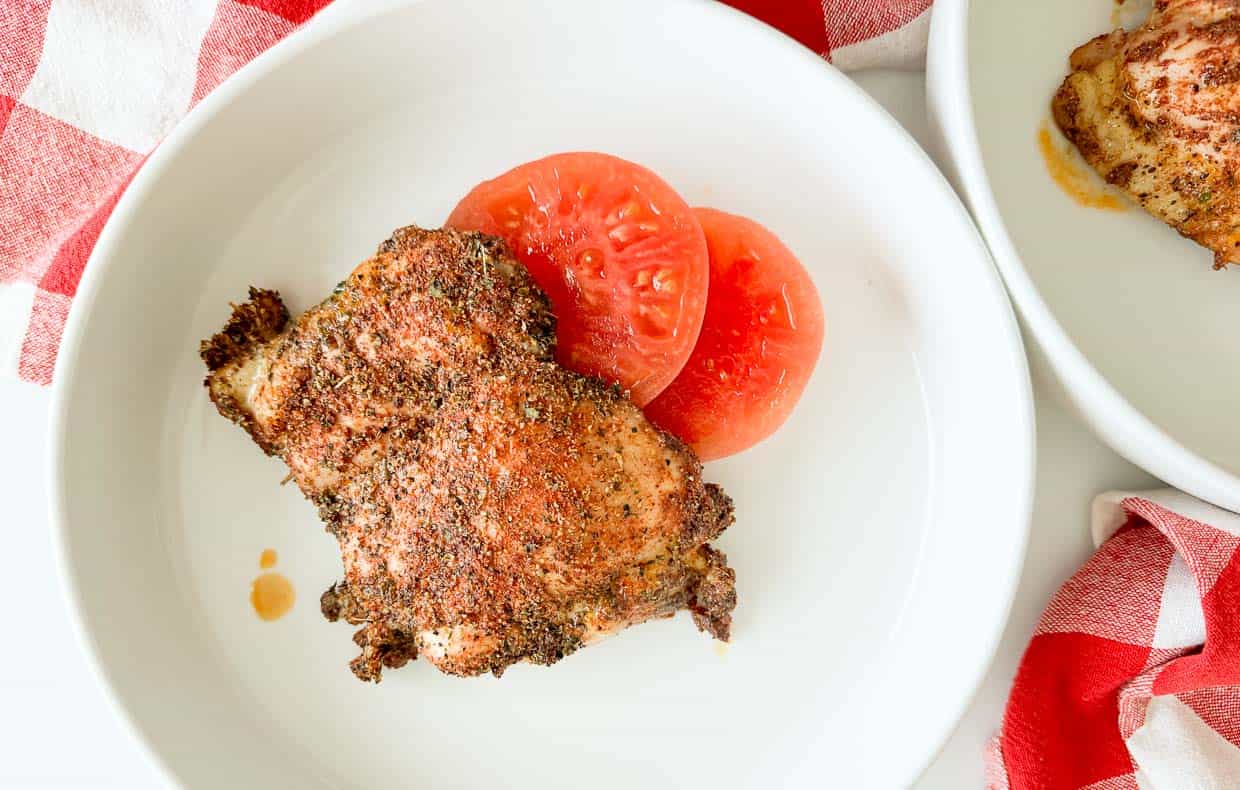 Chicken coated in seasoning on a plate with tomatoes.
