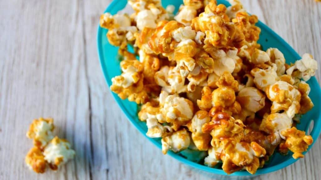 Bourbon caramel popcorn in a blue bowl on a wooden table.