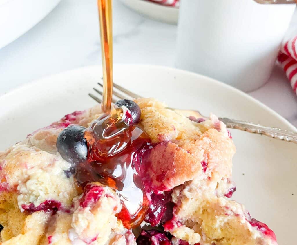 A plate of berry cobbler with syrup being poured over it.