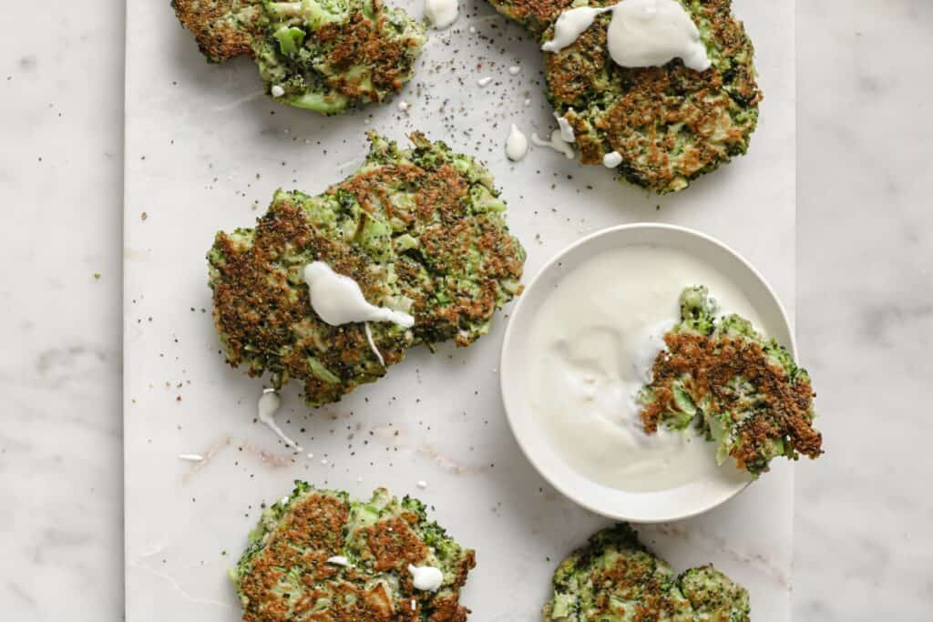 Broccoli fritters on a white plate with a bowl of sour cream.