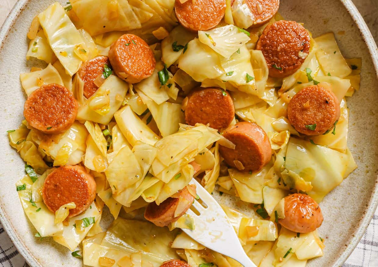 A pan of cabbage and sausage garnished with fresh herbs.