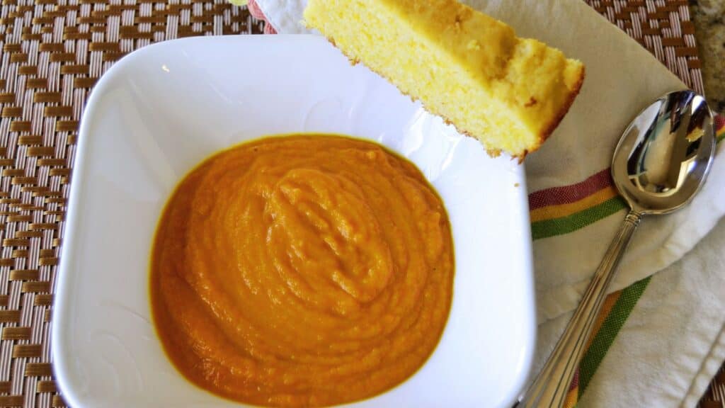 A bowl of carrot soup with bread and a spoon.