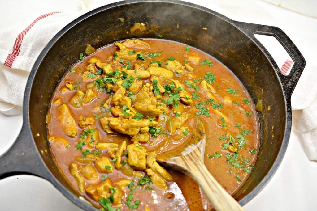 Chicken curry in a skillet with a wooden spoon.