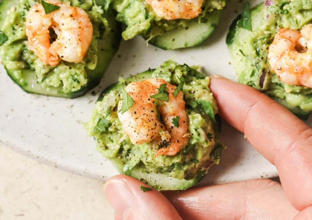 A person holding a cucumber with shrimp and guacamole.