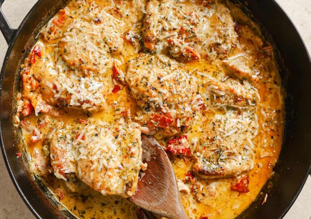 Chicken in a skillet with cheese and tomatoes.