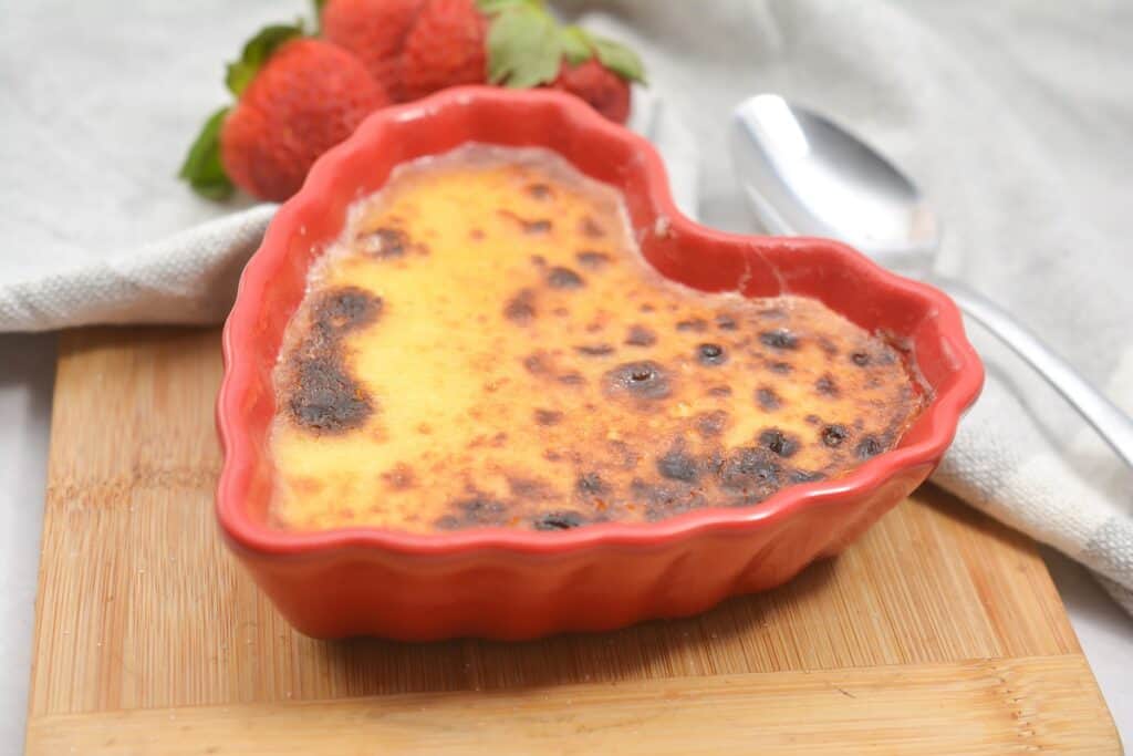 A red heart shaped dish with a spoon and strawberries.