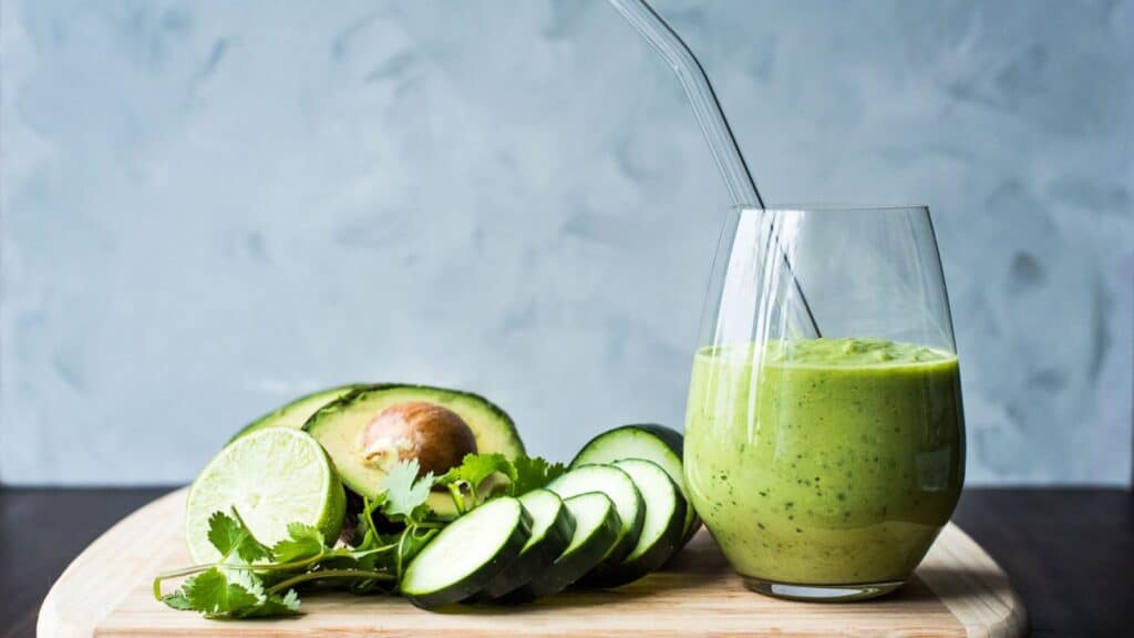 A green smoothie with cucumbers and limes on a wooden cutting board.