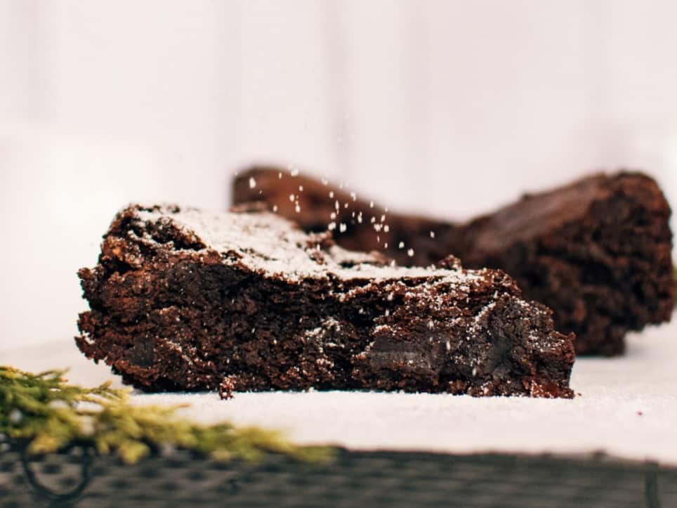 A mouthwatering chocolate brownie, sprinkled with powdered sugar, rests temptingly on a plate.