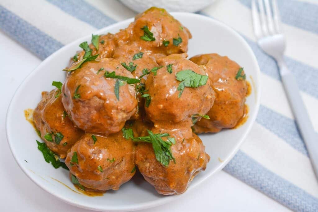 A bowl of meatballs with sauce and parsley.