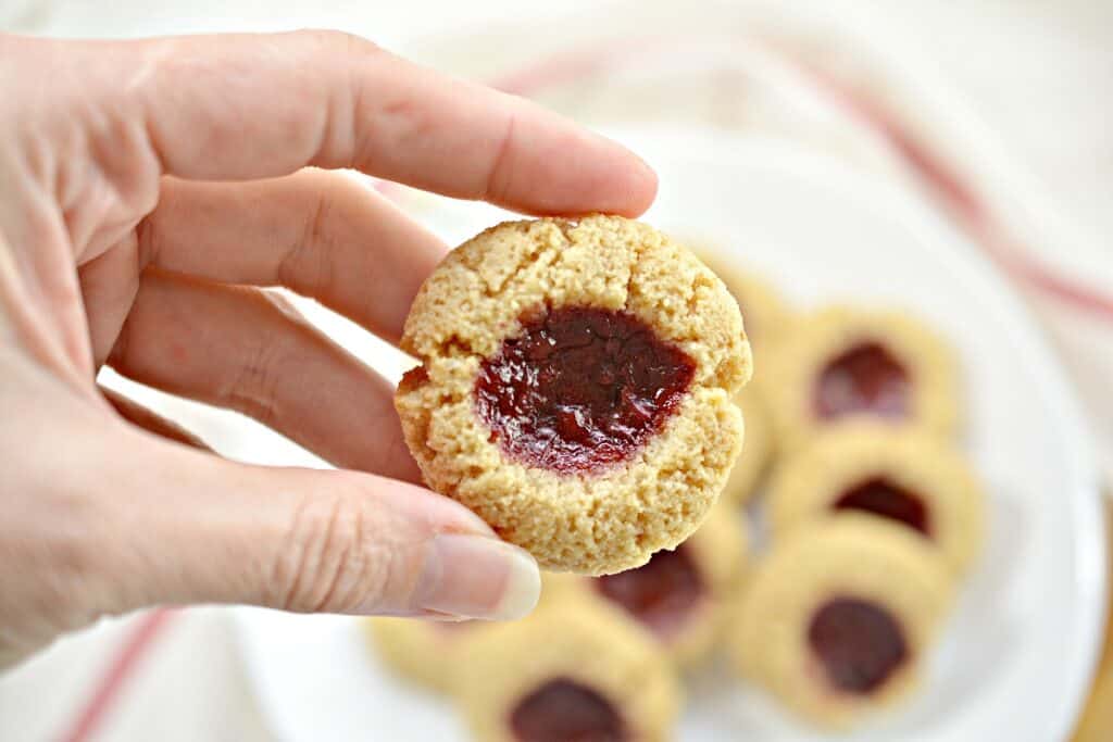 A person holding up a cookie with a jam filling.