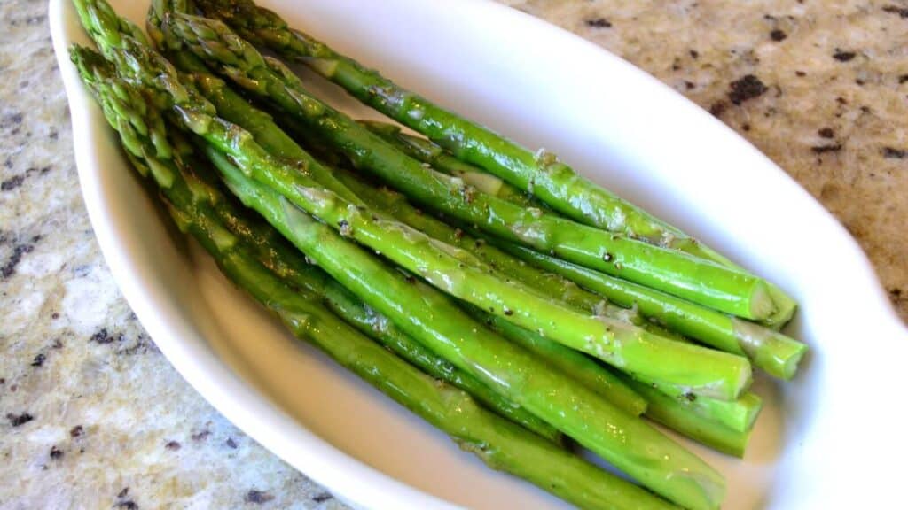 Asparagus spears in a white bowl on a granite counter.