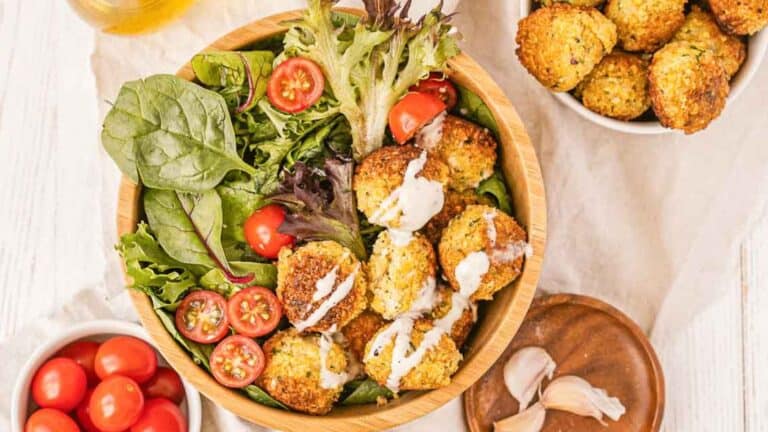 A bowl of falafel with tomatoes, lettuce, and dressing.