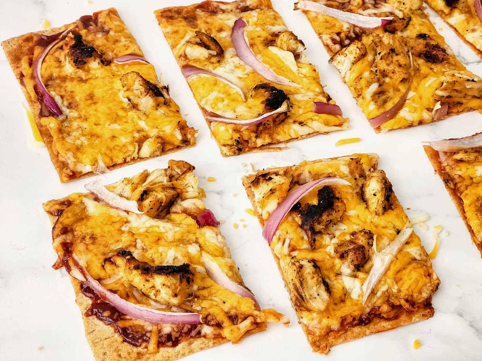 Grilled chicken flatbread pizzas on a marble countertop.