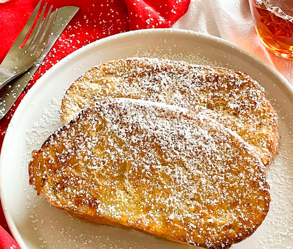 Two plates of french toast with powdered sugar on top.