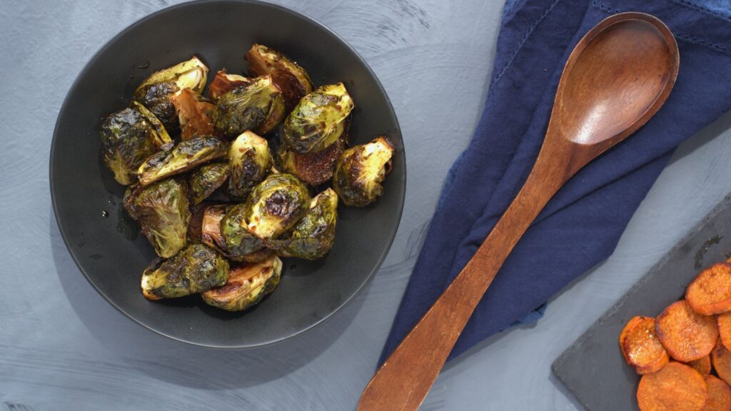 Roasted brussels sprouts on a plate with a wooden spoon.