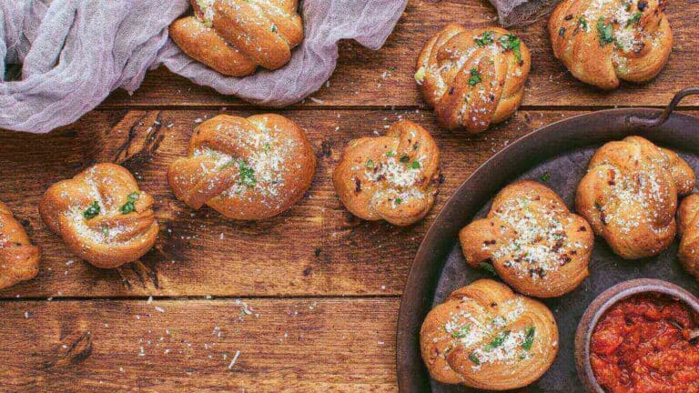 A plate of garlic knots and sauce on a wooden table.