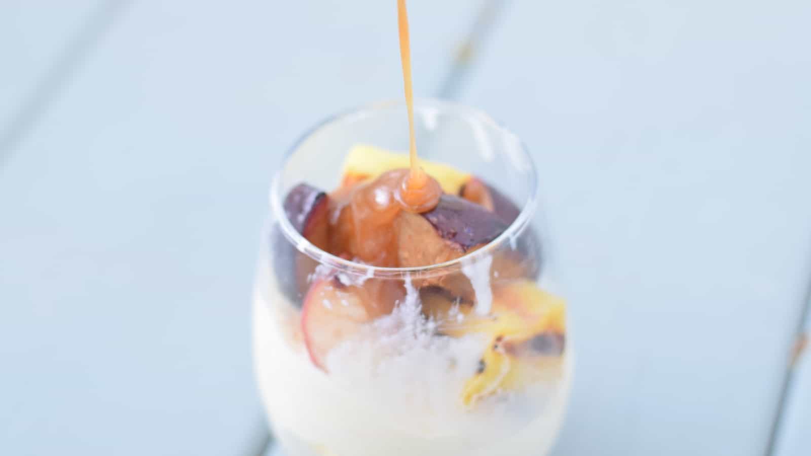 Image shows a glass with ice cream and grilled fruit having caramel drizzled into it.