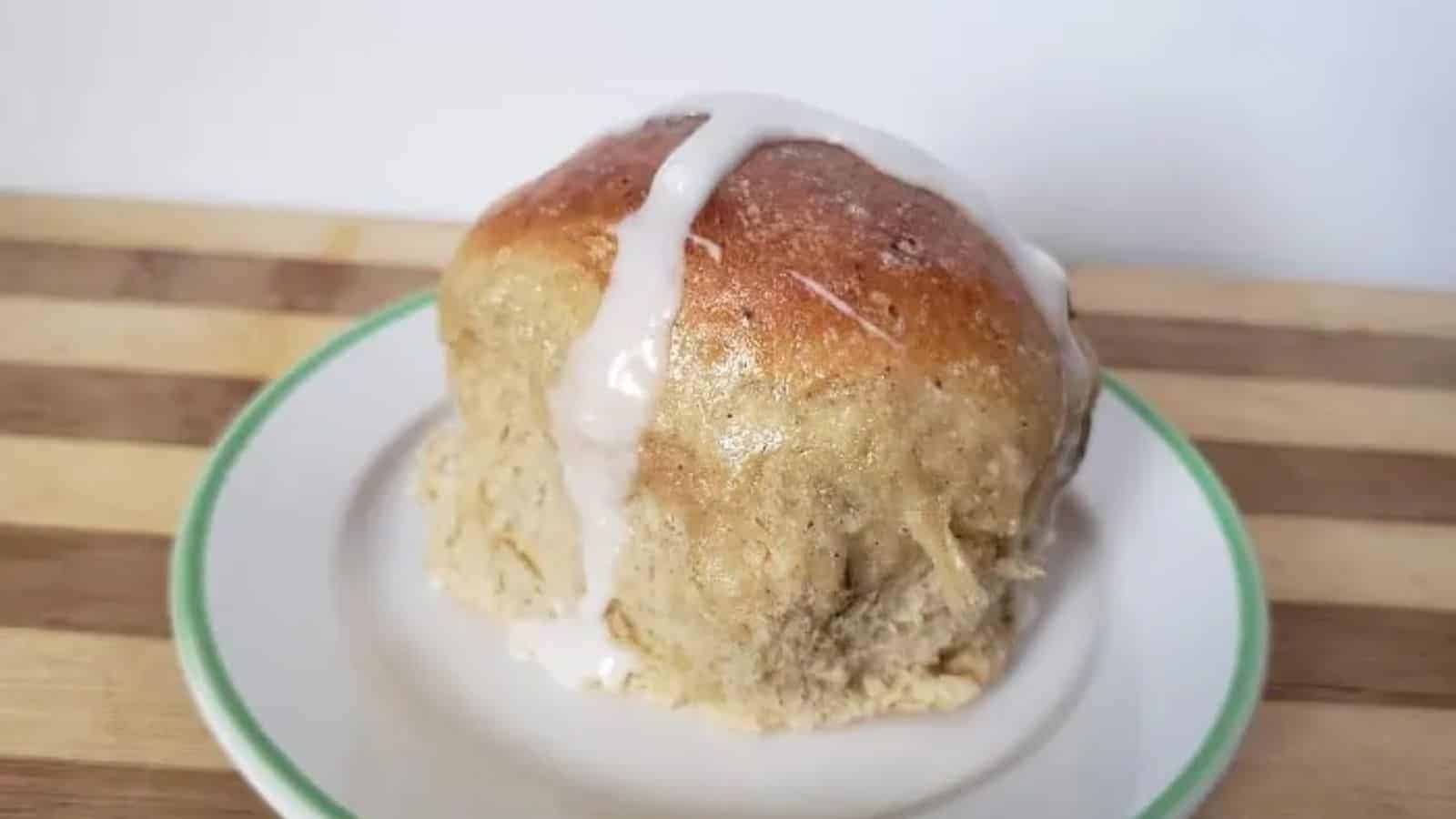 Image shows a hot cross bun with icing sitting on a plate.