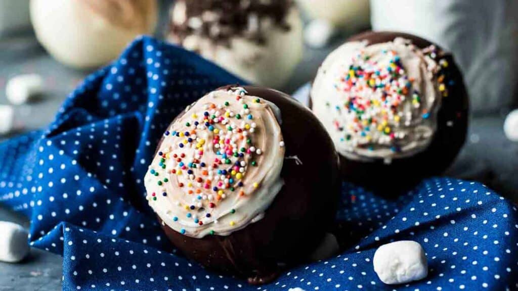 Hot chocolate bombs with sprinkles displayed on a vibrant blue cloth.