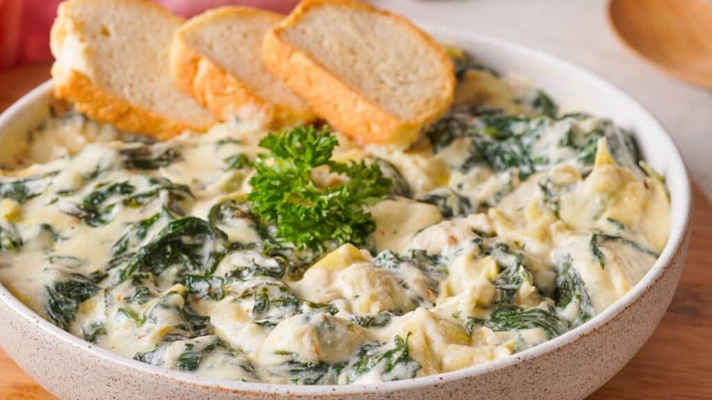 A bowl of spinach and artichoke dip with bread.