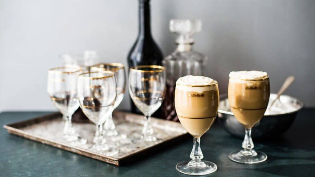 Two glasses of Irish cream coffee on a tray with a bar set up behind.