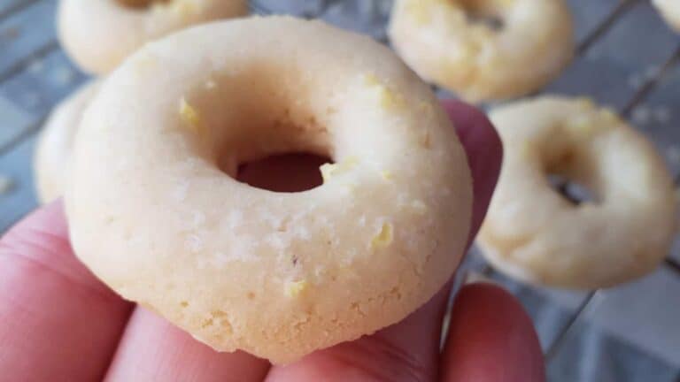 Image shows Baked lemon mini donuts held over more on a wire rack.