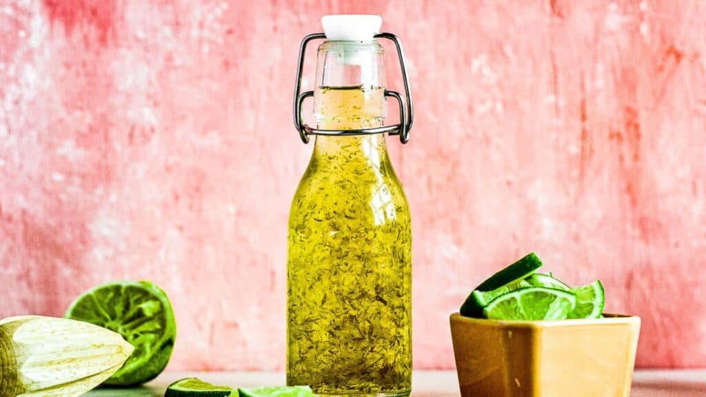 A bottle of olive oil and limes on a table.