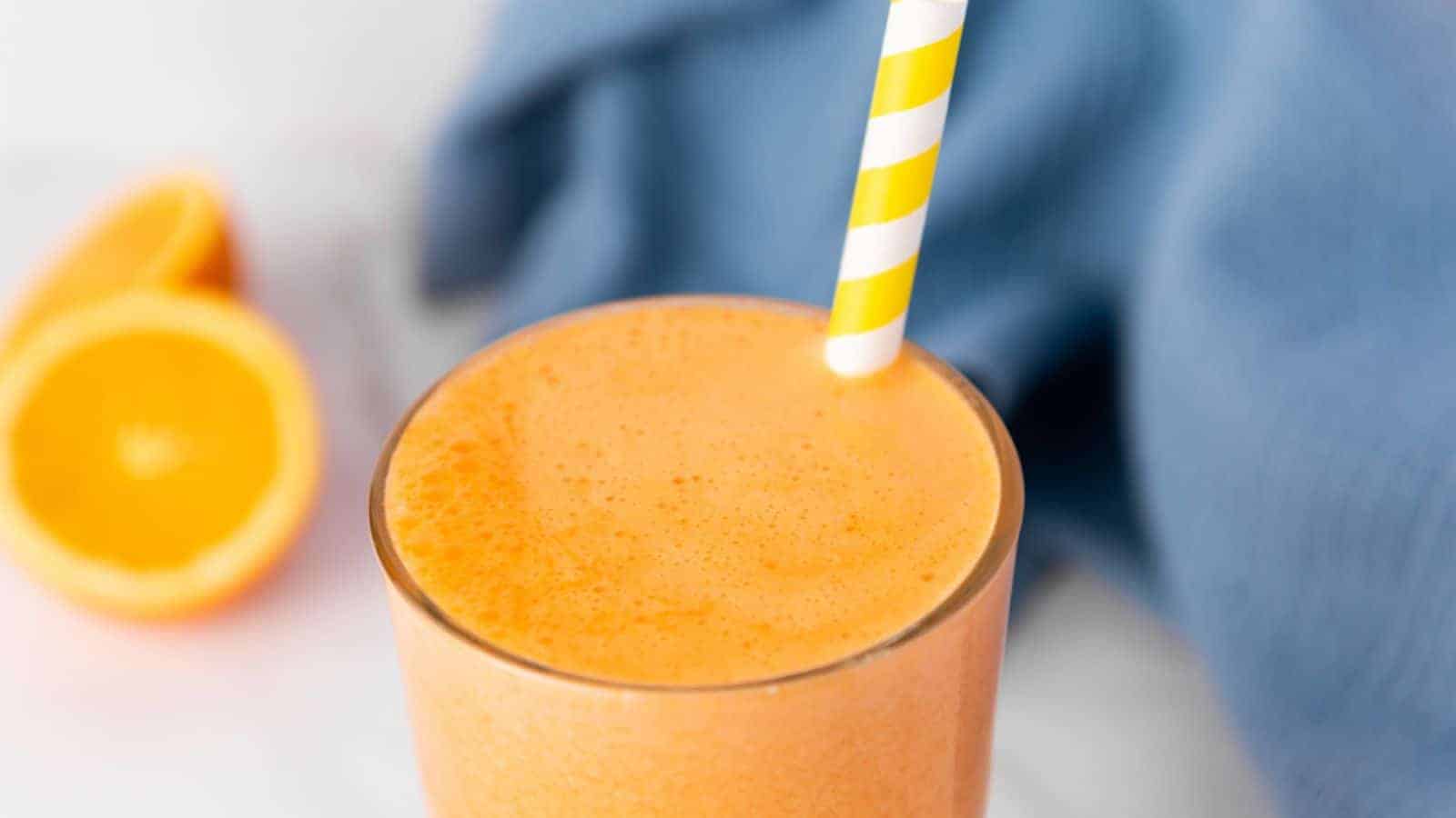 An orange smoothie with a striped straw.