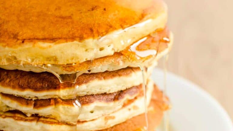 A stack of pancakes is being drizzled with syrup.