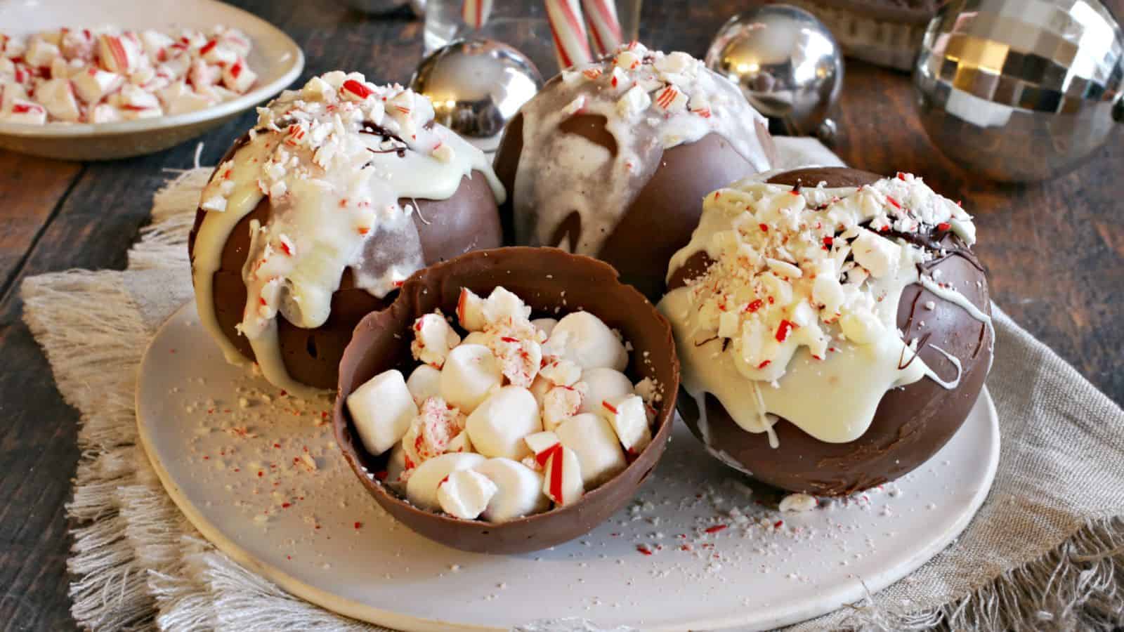 Four peppermint hot chocolate bombs on a plate, with an open hot chocolate bomb in the middle to show the inside.