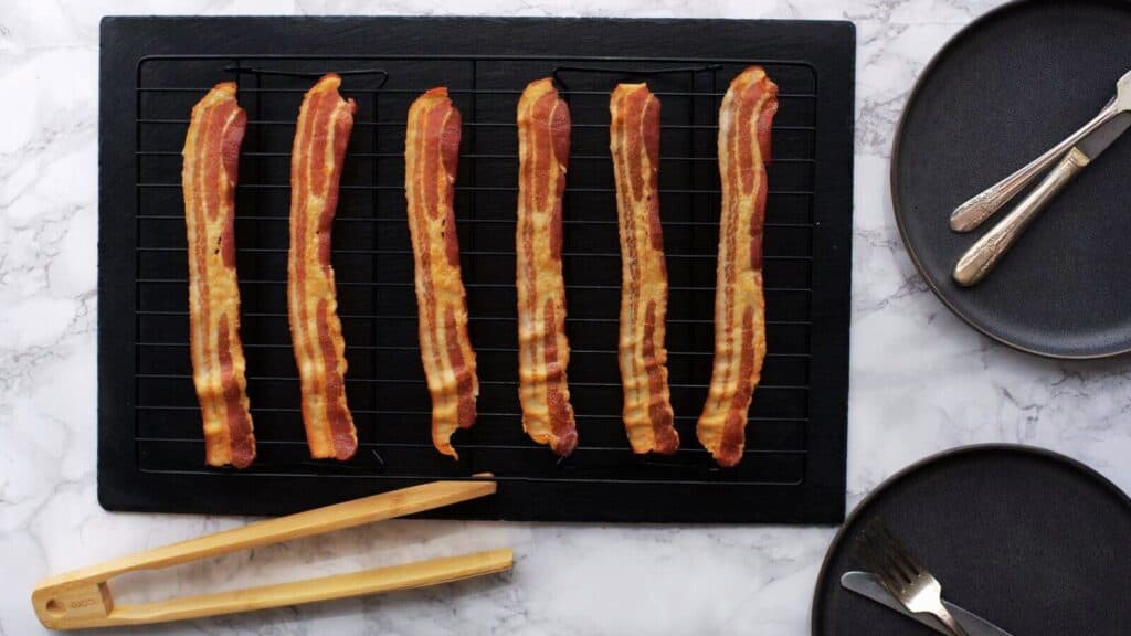 Bacon on a baking sheet with a knife and fork.