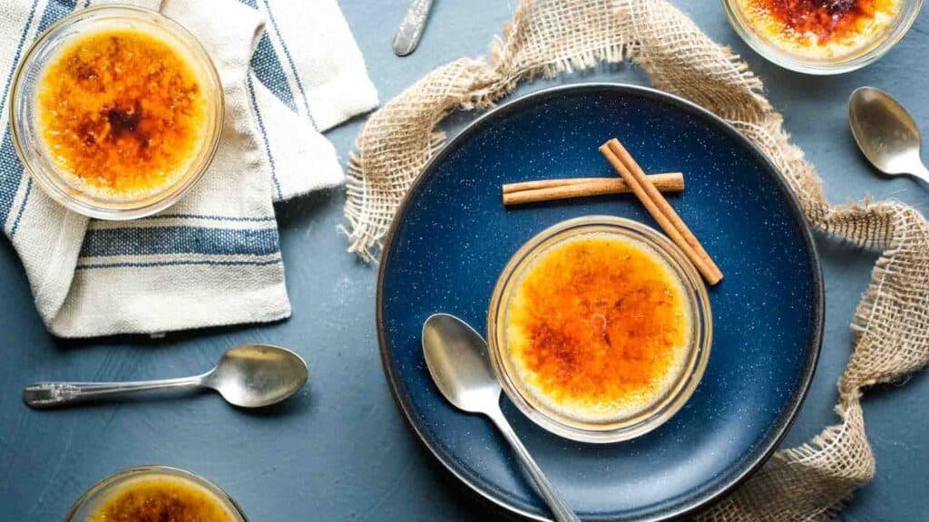 Creme brulee on a blue plate with cinnamon sticks.