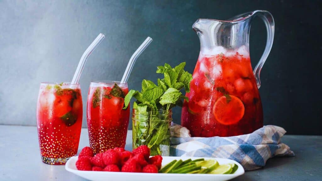 A pitcher of raspberry lemonade with limes and raspberries.