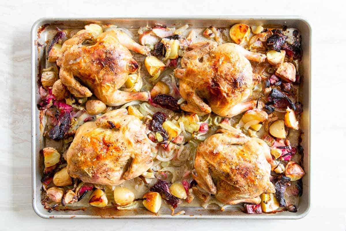 Cornish game hens on a baking sheet with vegetables.