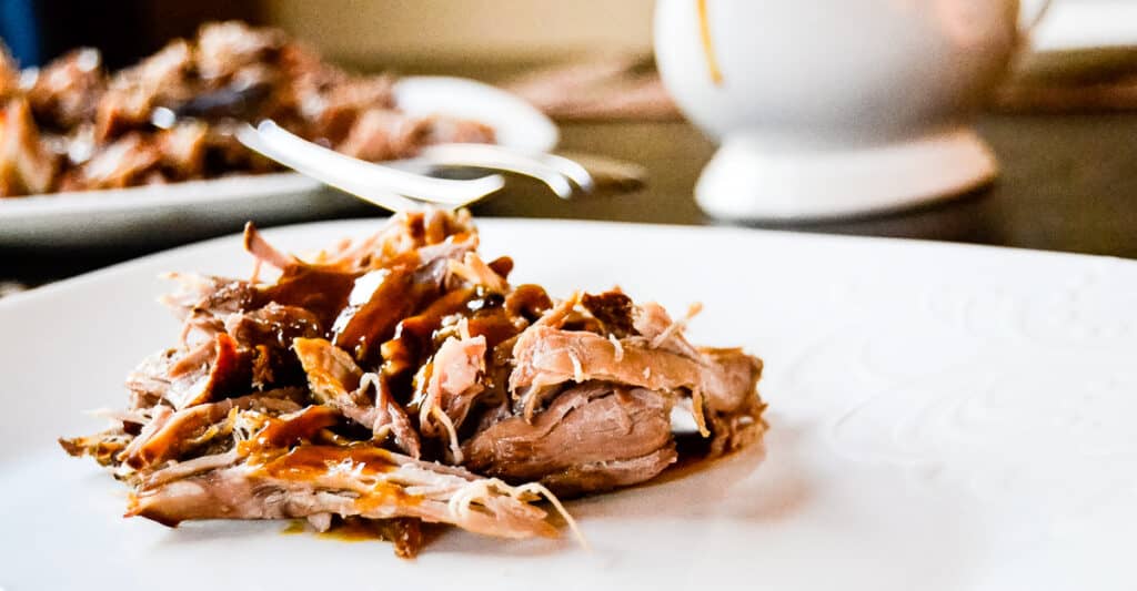 A plate of pulled pork with BBQ sauce with a fork on it.