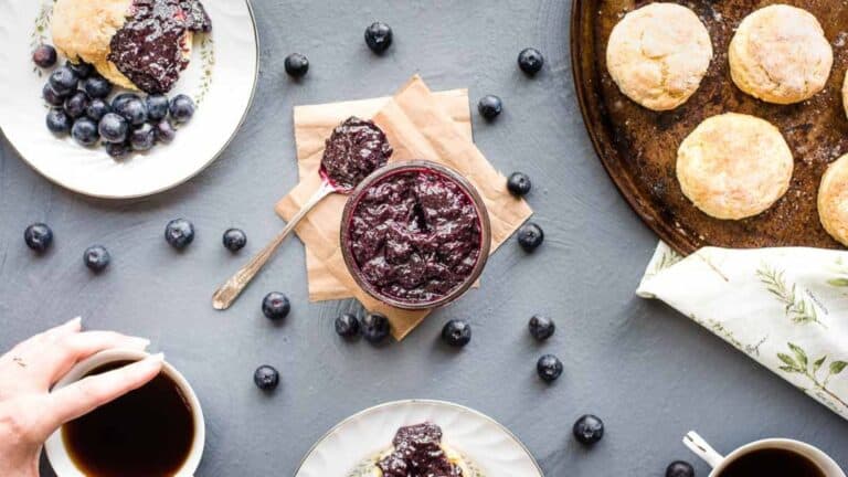 A plate of blueberry scones with blueberry jam and a cup of coffee.