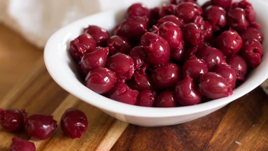 Cherries in a white bowl on a cutting board.