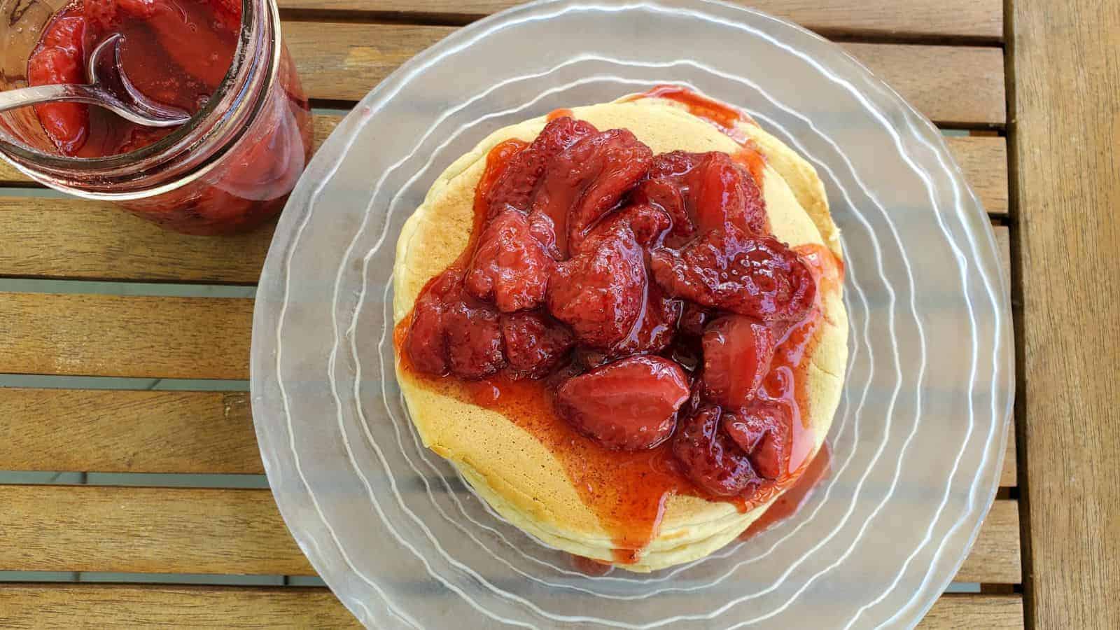 Image shows an overhead shot of Sourdough Pancakes on a plate with strawberry syrup dousing them.