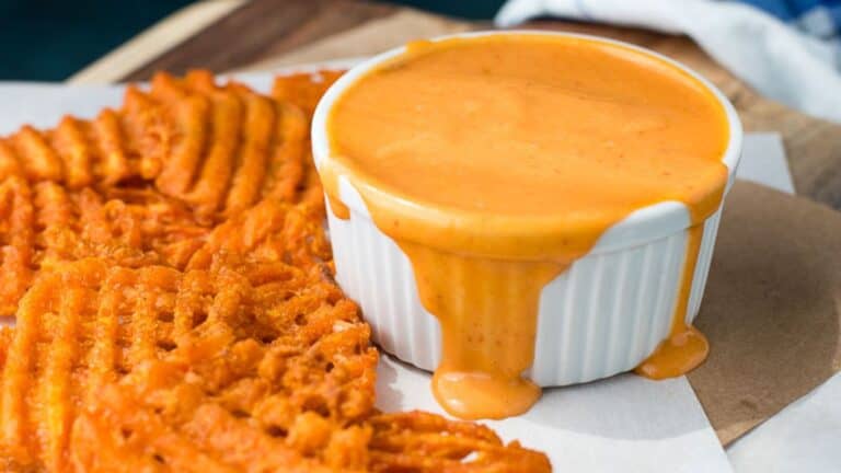 A bowl of sweet potato fries with a cup of spicy sweet sriracha sauce.