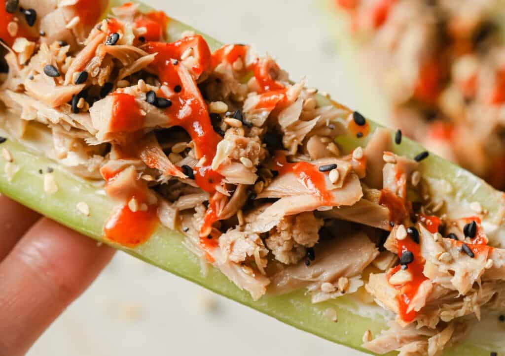 A person is holding a cucumber with tuna and sesame seeds on it.