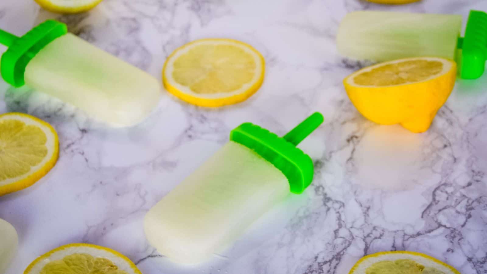 Spiked lemonade popsicles on a marble background next to lemons.
