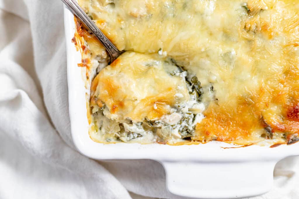 Cheesy spinach casserole in a white dish with a spoon.