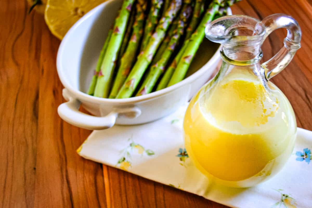 A jar of hollandaise sauce next to a bowl of asparagus.