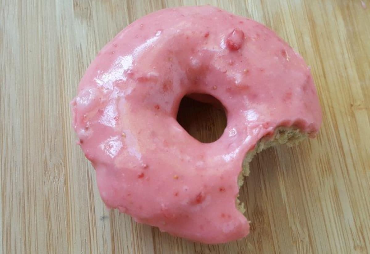 Image shows a freshly dipped strawberry donut held over the glaze.
